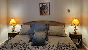 A bedroom with a wooden ceiling, a bed with a floral bedspread, two nightstands with lamps, and a framed picture on the wall.