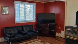 A living room with a black leather sofa, a flat-screen TV on a wooden stand, a fireplace, and a window with blinds.