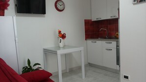 Een knus woongedeelte met een kitchenette, een eettafel, een rode bank en een wandtelevisie.