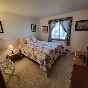 Un dormitorio con una cama, una mesita de noche con lámpara, un escritorio con teléfono y una ventana con cortinas.