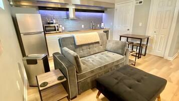 Eine moderne Küche mit grauem Sofa, Hocker, einem kleinen Tisch und einer Mikrowelle.