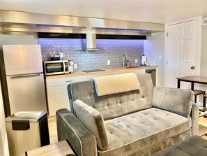 A modern kitchen with a grey sofa, a microwave, a refrigerator, and a sink. - Snuggle into Sweet Seclusion (Cheyenne)