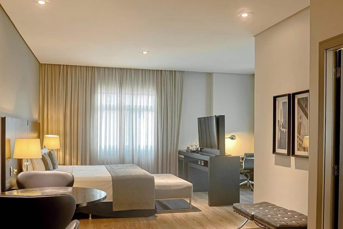 A hotel room with a bed, desk, chair, and a television.