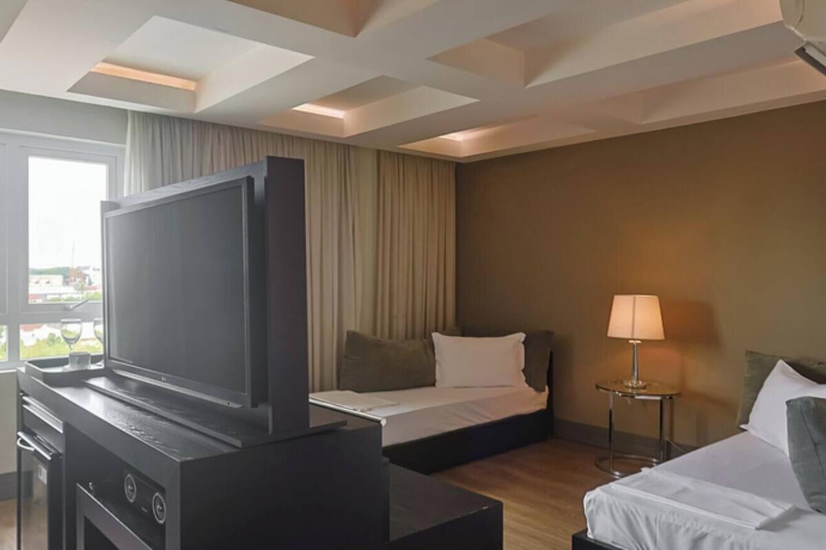 A hotel room with a TV, two beds, a desk, and a window with curtains.