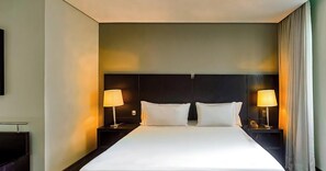A hotel room with a large bed, two bedside tables with lamps, and a headboard. - Manhattan Floor By 1/4 UmQuarto | Ao lado do Shopping Estação (Curitiba)