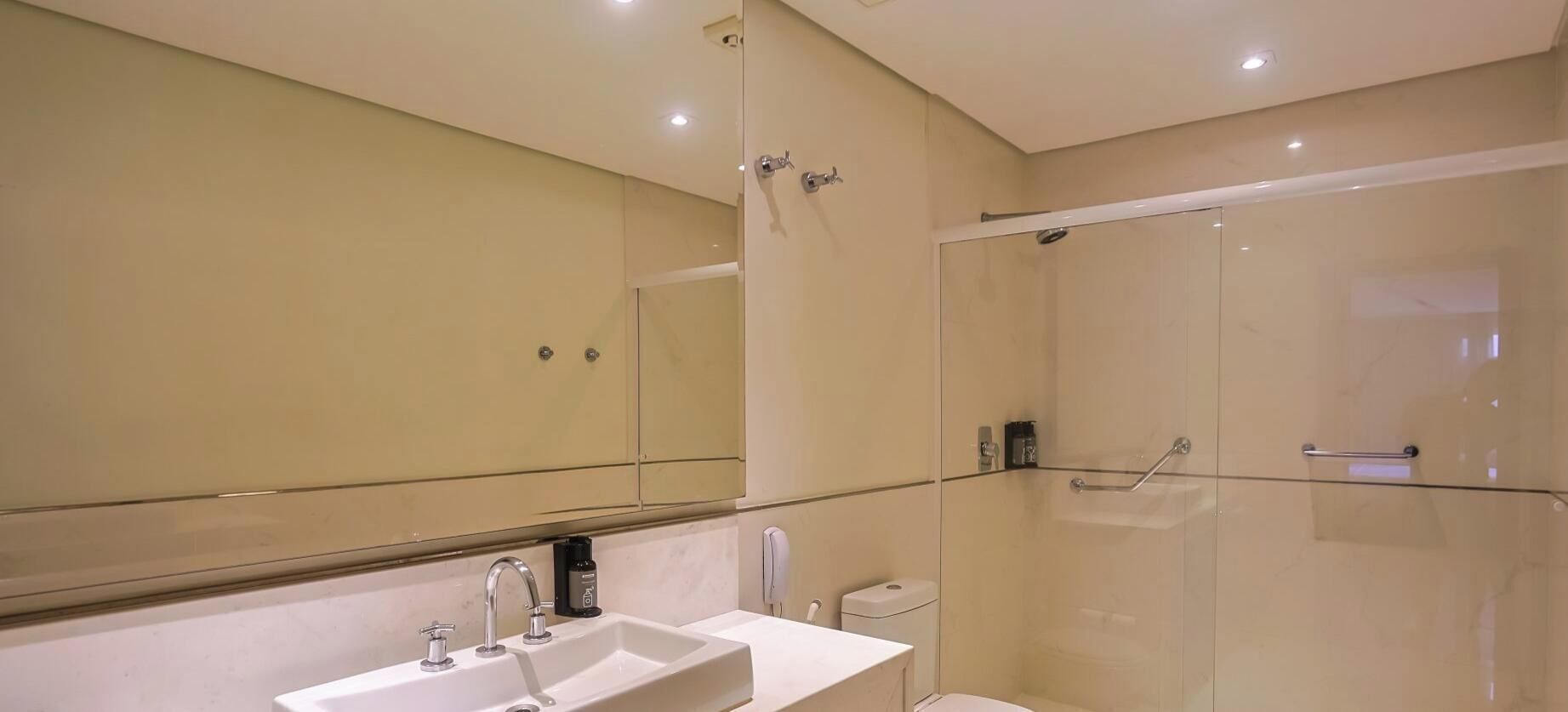 Uma casa de banho moderna com cabine de duche em vidro, lavatório branco e um espelho grande.
