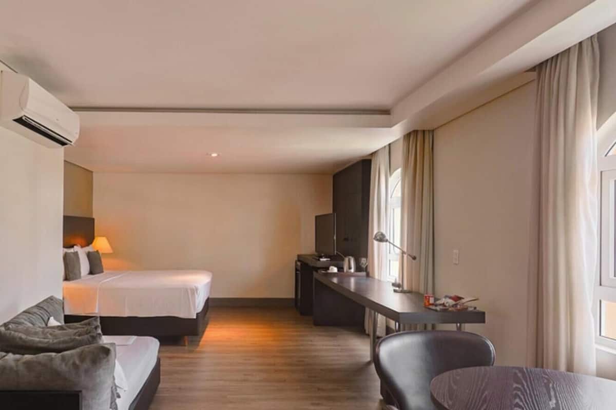 A hotel room with a bed, a desk, a chair, a sofa, and a large window.