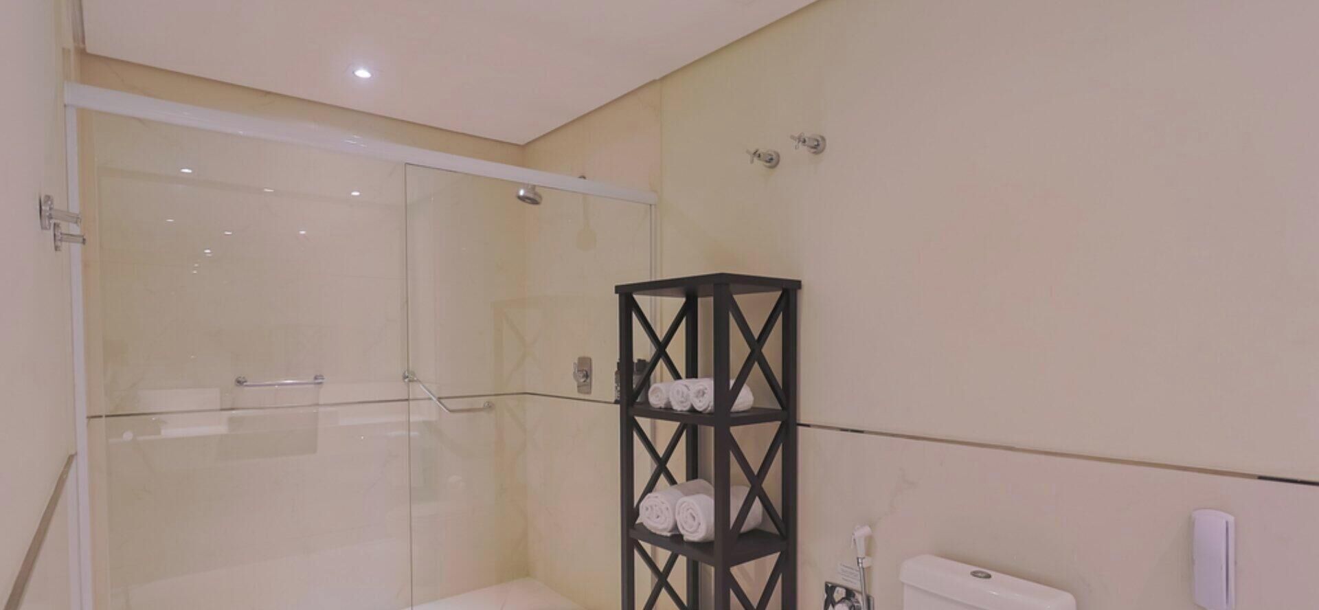 Un baño con cabina de ducha de vidrio, un toallero negro y un inodoro.
