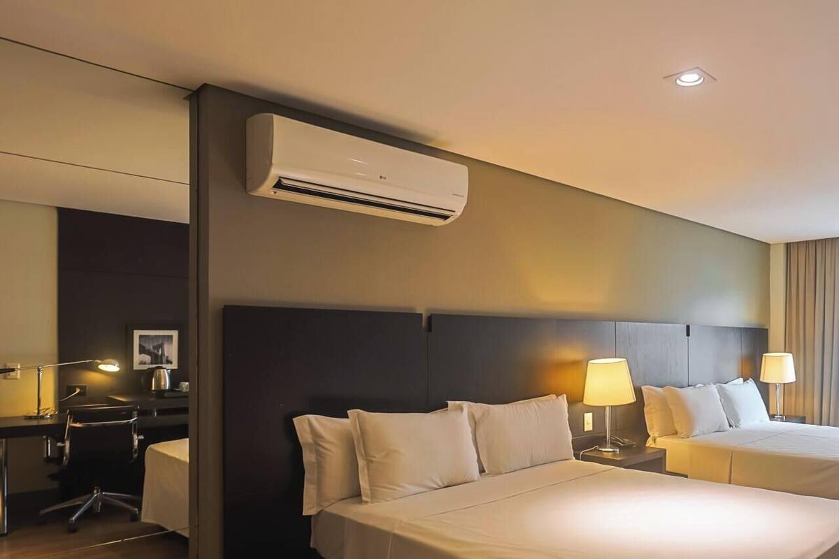 A hotel room with two beds, a desk, a chair, an air conditioner, and a window with curtains.