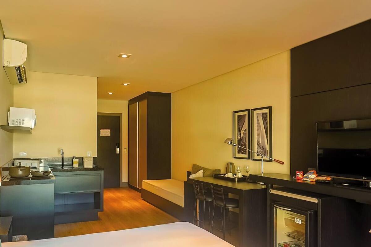 A hotel room with a bed, a desk, a kitchenette, and a TV.