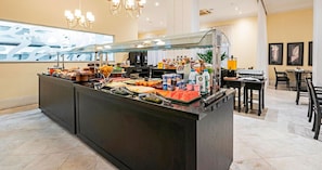 A buffet area with a variety of food items and beverages, a seating area with tables and chairs, and a chandelier. - Manhattan On Floor (Curitiba)