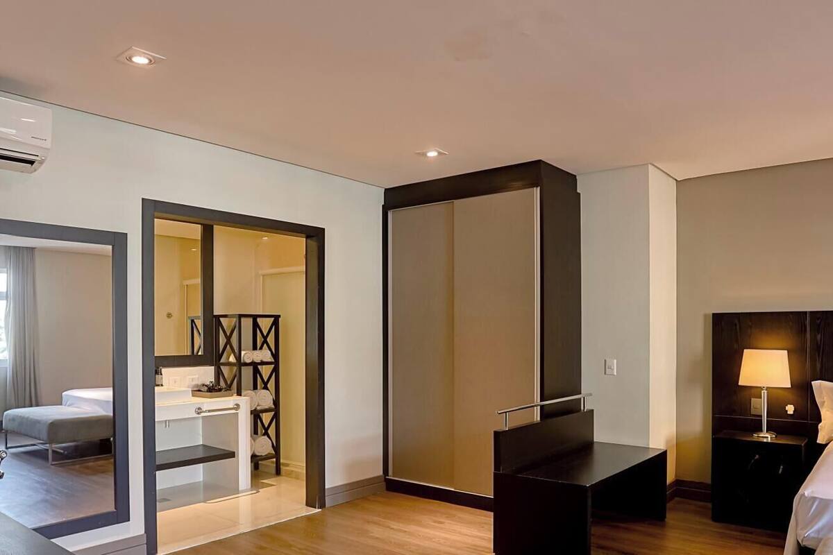 A modern hotel room with a bed, bedside table, lamp, and a large mirror.