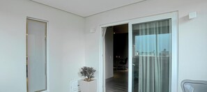 Quarto de hotel moderno com porta de correr de vidro que dá para uma varanda, um pequeno vaso de planta e uma cadeira.