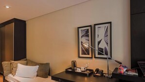 A hotel room with a bed, a desk with a lamp, a telephone, and two framed pictures on the wall. - Manhattan On Floor (Curitiba)