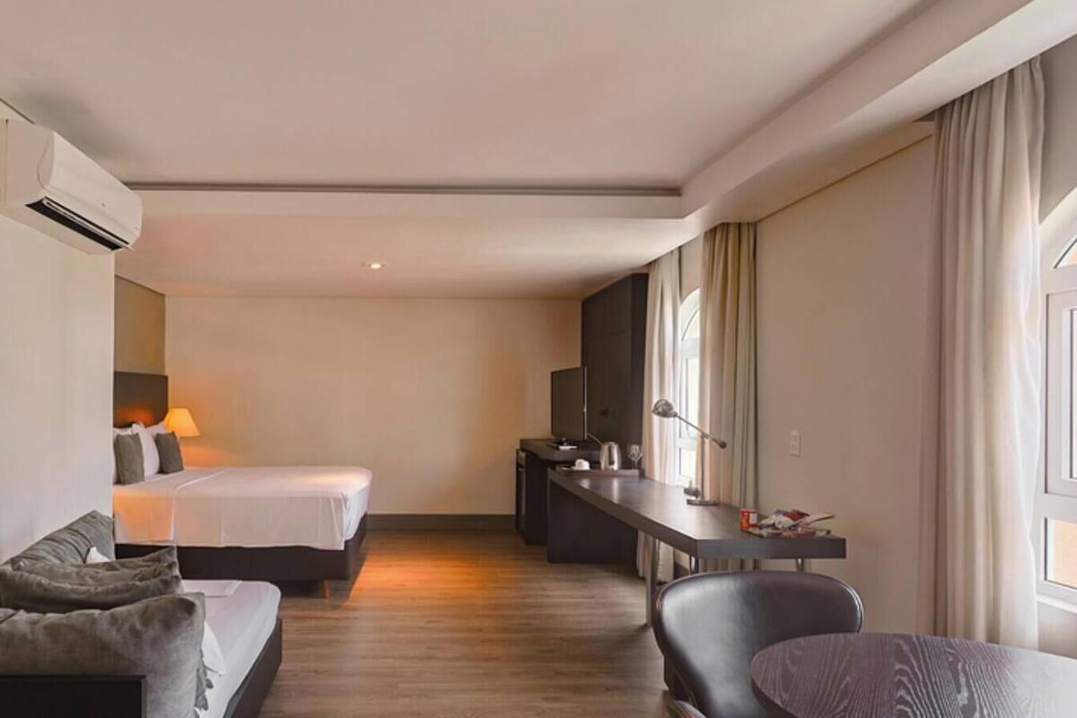 A modern hotel room with a bed, a sofa, a desk, and a dining table.