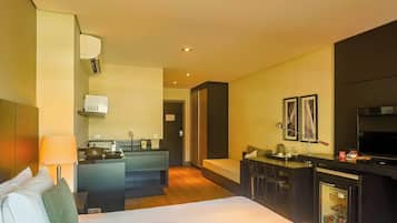 A hotel room with a bed, a kitchenette, a TV, and a seating area.
