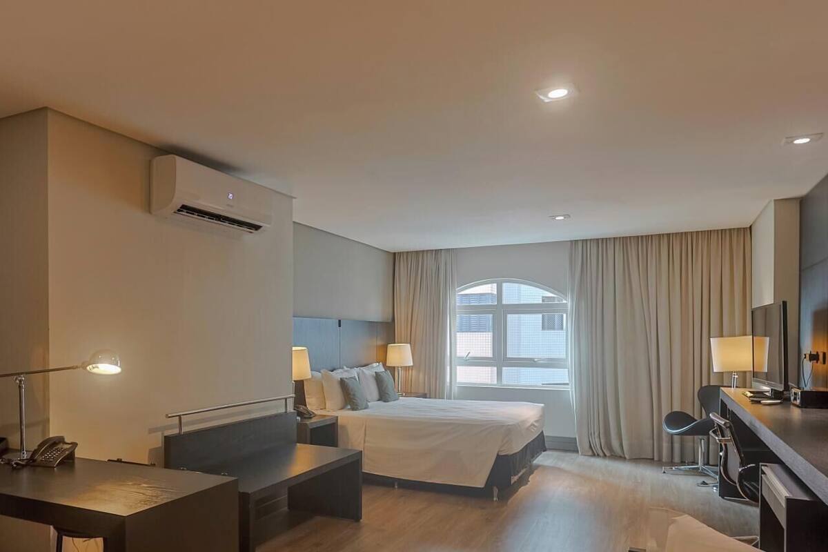 A hotel room with a bed, desk, and kitchenette.
