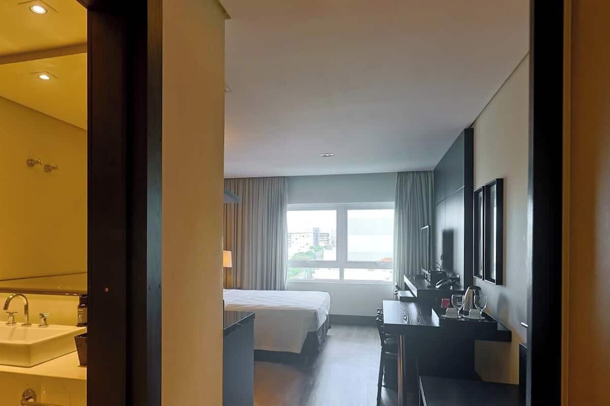 A hotel room with a bed, a desk, a chair, a sink, and a window with a view.