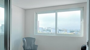 A room with a large window, a chair, and a door. - Manhattan On Floor (Curitiba)