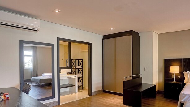 A modern hotel room with a bed, bedside table, lamp, and a view of the bathroom. - Manhattan On Floor (Curitiba)
