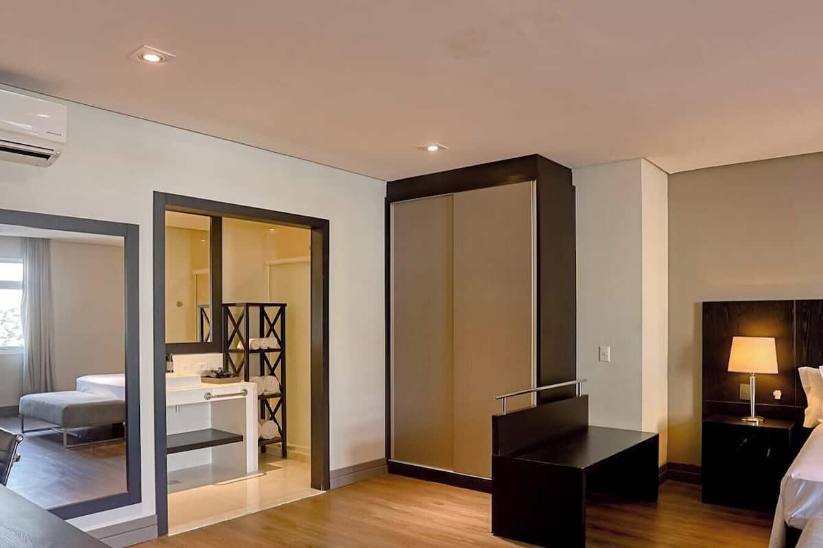 A modern hotel room with a bed, bedside table, lamp, and a view of the outside.