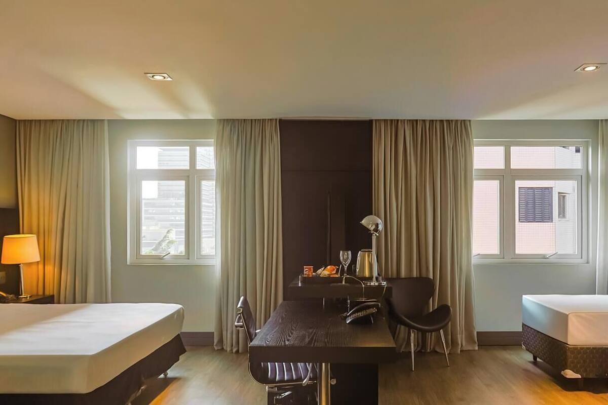 A hotel room with two beds, a desk, a chair, and a window.