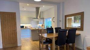 A modern kitchen with white cabinets, a stainless steel range hood, and a dining area with a wooden table and black chairs. - Luxury 2 bed Apartment Golden Triangle w Parking (Norwich)
