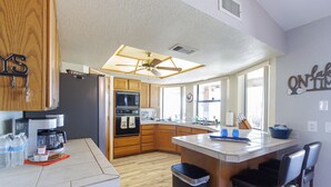 Eine moderne Küche mit Holzausstattung, einer zentralen Kochinsel mit Barhocker, einem Deckenventilator und einem großen Fenster für natürliches Licht.