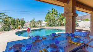 Ein Essbereich am Pool mit Tisch für vier Personen, mit Blick auf einen Swimmingpool und Palmen.