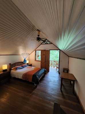 A bedroom with a sloped ceiling, a bed with a colorful quilt, a ceiling fan, and a view of the outdoors through a door.