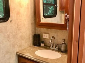 A compact bathroom with a sink, faucet, and a window above the mirror.