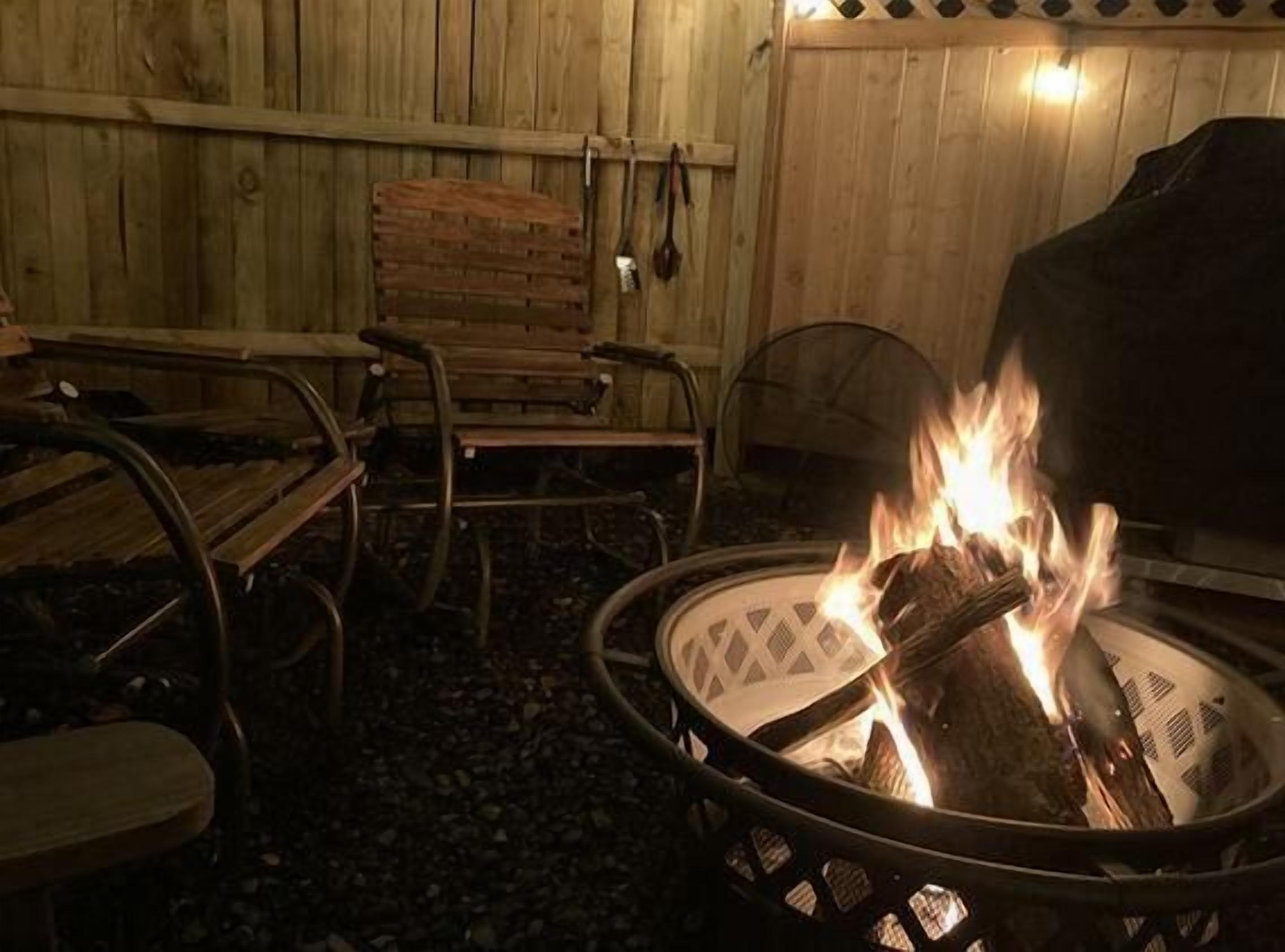 Een vuurkorf met brandhout, omringd door metalen stoelen en een bank.