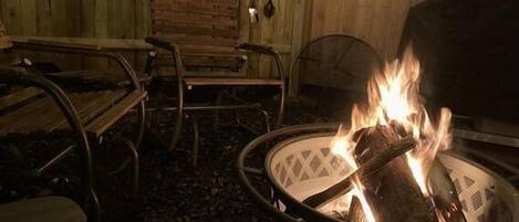 Een vuurkorf met brandhout, omringd door metalen stoelen en een bank.