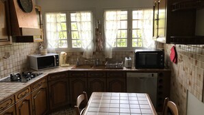 A kitchen with a tiled backsplash, wooden cabinets, a stove, a microwave, a toaster, and a sink. - House (Hourtin)