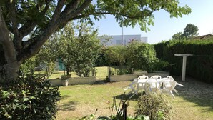 A garden with white plastic chairs, a large tree, and various plants. - House (Hourtin)