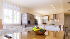 Een moderne keuken met een glazen eettafel, witte kasten en een schaal met fruit.