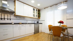 Une cuisine moderne avec des armoires blanches, une hotte de cuisinière en acier inoxydable, un four à micro-ondes et un lave-vaisselle. On y trouve également un coin repas avec une table ronde et des chaises orange.