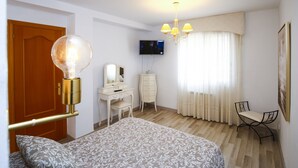 Une chambre à coucher comprenant un lit, une commode, un bureau, une chaise, un téléviseur et un lustre.