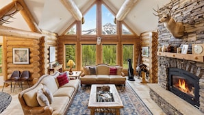 A log cabin interior with a stone fireplace, wooden furniture, and a mountain view.