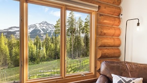A log cabin interior with a large window offering a mountain view.