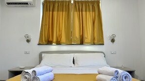 Habitación de hotel con cama, dos mesitas de noche, aire acondicionado de pared y ventana con cortinas amarillas.