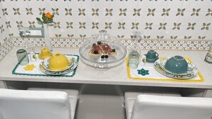 Una encimera de cocina con un desayuno que incluye un tazón amarillo, un tazón de vidrio con bayas, una tetera verde y una jarra de vidrio.