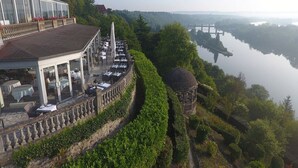 Een restaurant aan de rivier met terras, met uitzicht op een rustig rivierlandschap en een brug in de verte.