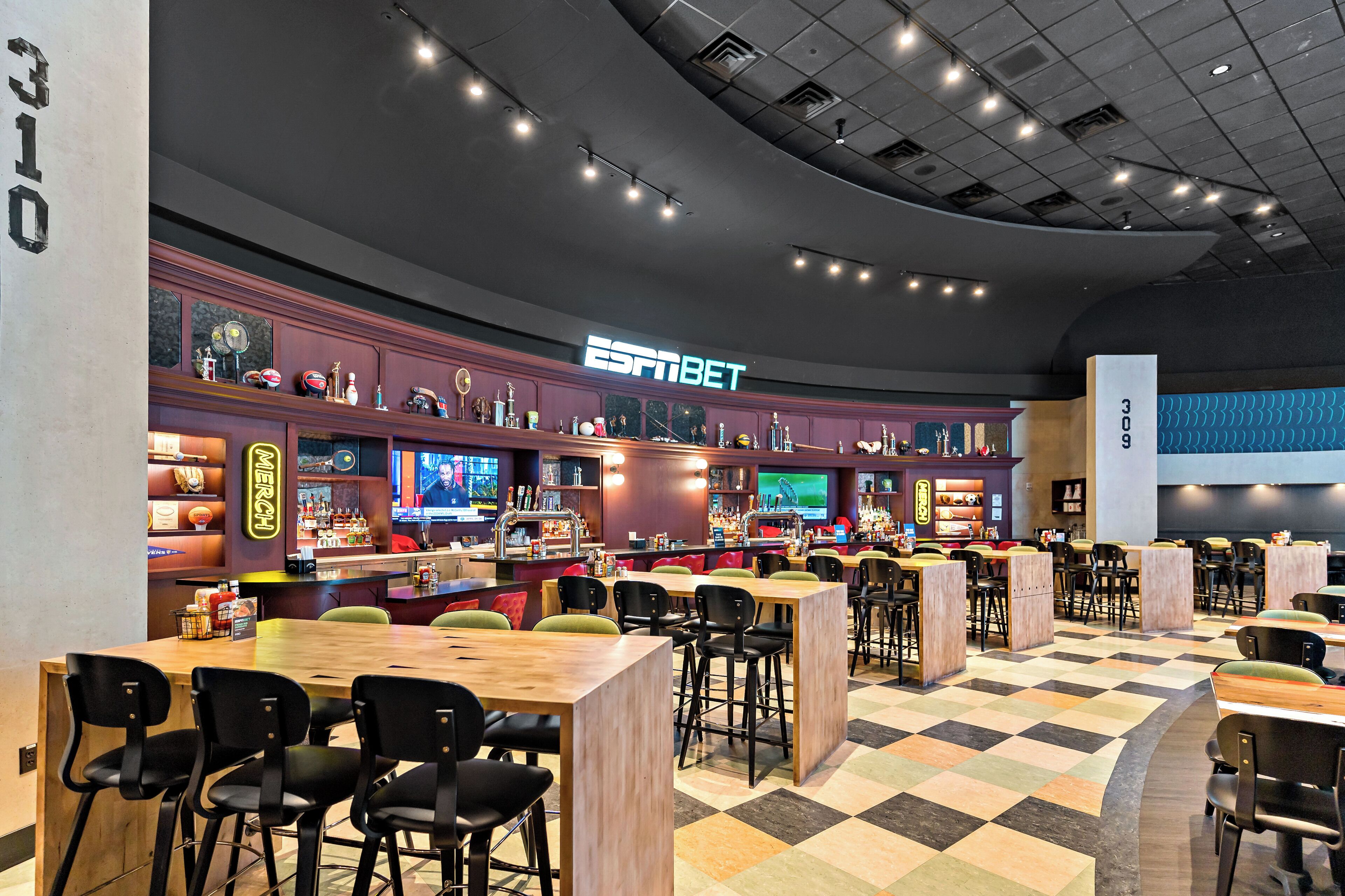 Eine Sportsbar mit mehreren Sitzbereichen, einer Bar und einer großen Leinwand, die Sportübertragungen zeigt.