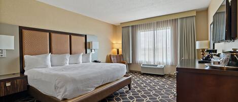 Una habitación de hotel con una cama grande, un escritorio, un televisor y una ventana con cortinas.