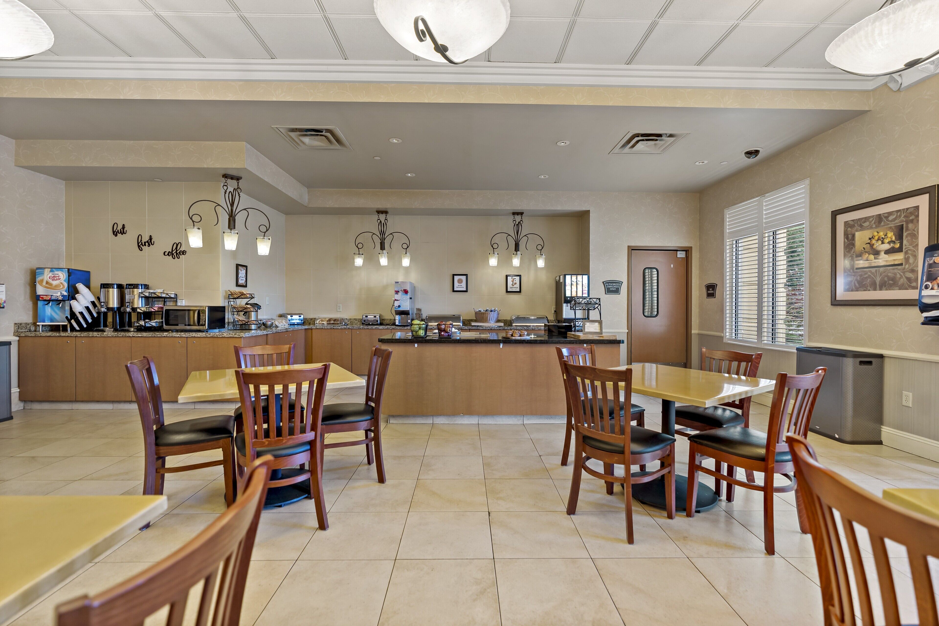 A spacious dining area with wooden tables and chairs, a central island with kitchen appliances, and pendant lighting.