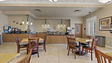 A spacious dining area with wooden tables and chairs, a central island with kitchen appliances, and pendant lighting.