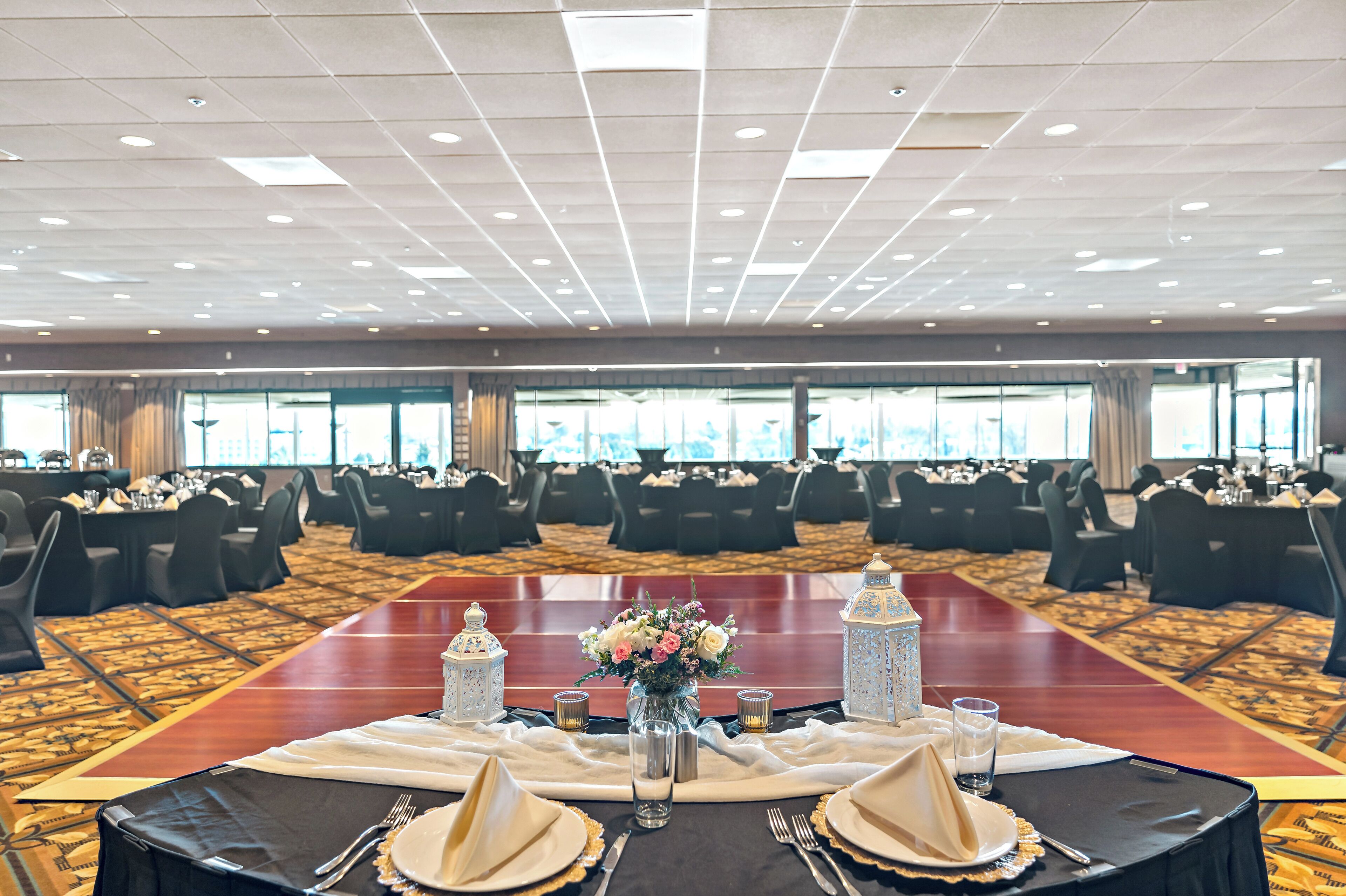 A banquet hall with round tables set for a formal event, featuring a central floral arrangement and decorative lanterns.