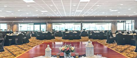 A banquet hall with round tables set for a formal event, featuring a central floral arrangement and decorative lanterns.