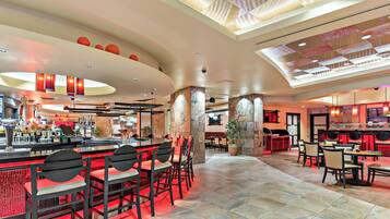 Een ruim restaurant met hoge plafonds, een centraal gelegen bar en diverse zithoeken.